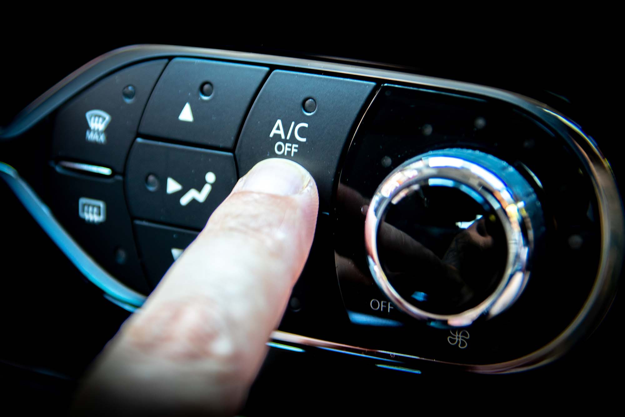 A finger pressing the A/C or air conditioning button on the dashboard of a car